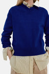 Pull col V bleu de MANGO, tricot fin, porté sur chemise à fines rayures jaunes, vue de face.