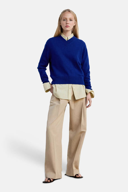 Pull col V bleu de MANGO, tricoté, porté sur chemise jaune pâle, vue de face, pantalon beige et sandales noires