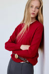 Pull col V rouge de MANGO, coupe ample, porté avec ceinture marron et pantalon gris, vue de face.