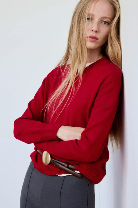 Pull col V rouge de MANGO, coupe ample, porté avec ceinture marron et pantalon gris, vue de face.