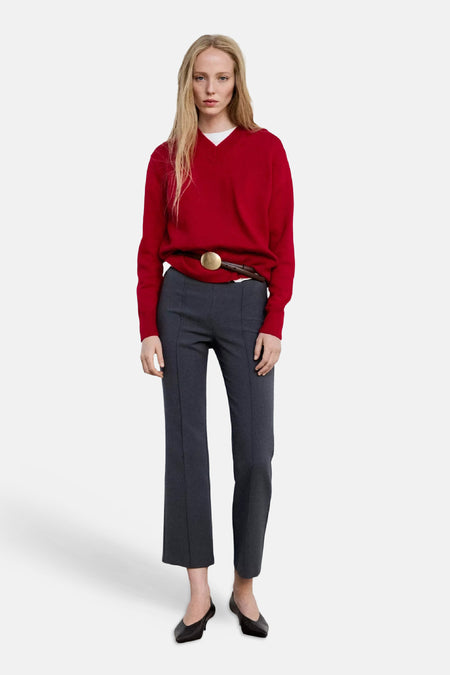 Pull col V rouge de MANGO, porté avec pantalon gris et ceinture à boucle dorée, vue frontale lifestyle