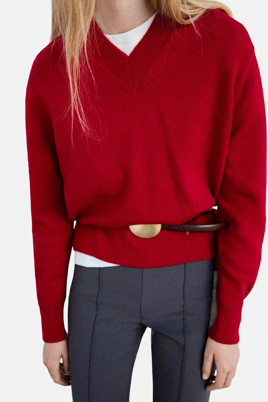 Pull col V rouge de MANGO, tricoté, porté avec ceinture marron et pantalon gris, vue de face.