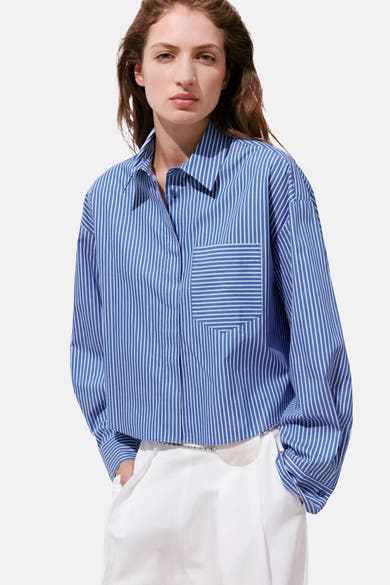 Blue and white striped long-sleeve blouse with chest pocket, worn with white pants, front view