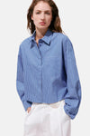 Blue and white striped long-sleeve blouse with chest pocket, worn with white pants, front view