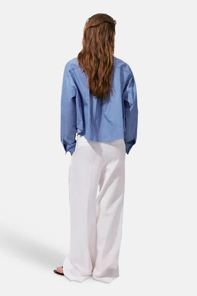 Multicolored long-sleeve blouse with blue and white vertical stripes, back view, worn with white wide-leg pants and black sandals
