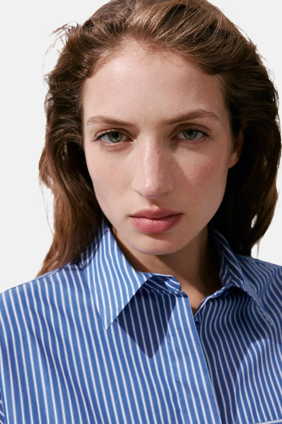 Multicolored long-sleeve blouse with blue and white vertical stripes, classic collar, front button closure, close-up view on model