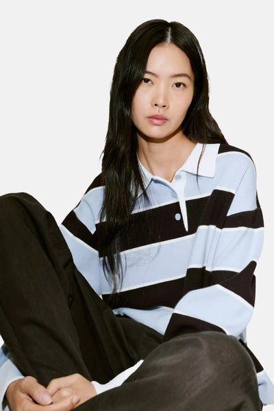 Multicolored striped knit polo sweater with white collar and buttons, worn by model in relaxed pose, paired with dark pants.