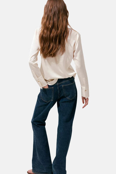 Ecru long-sleeve blouse with smooth fabric and buttoned cuffs, back view on model wearing dark blue flared jeans