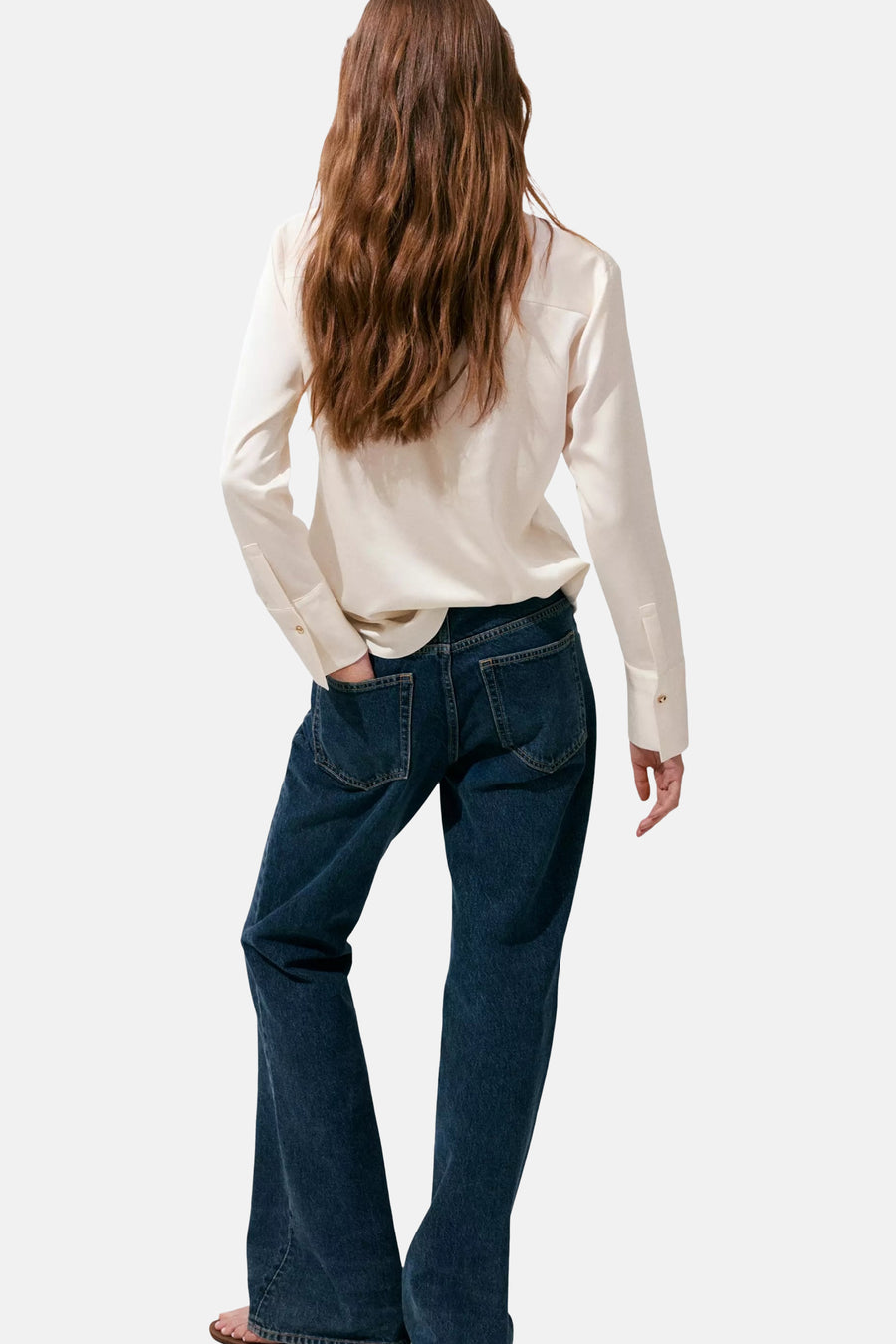 Ecru long-sleeve blouse with smooth fabric and buttoned cuffs, back view on model wearing dark blue flared jeans