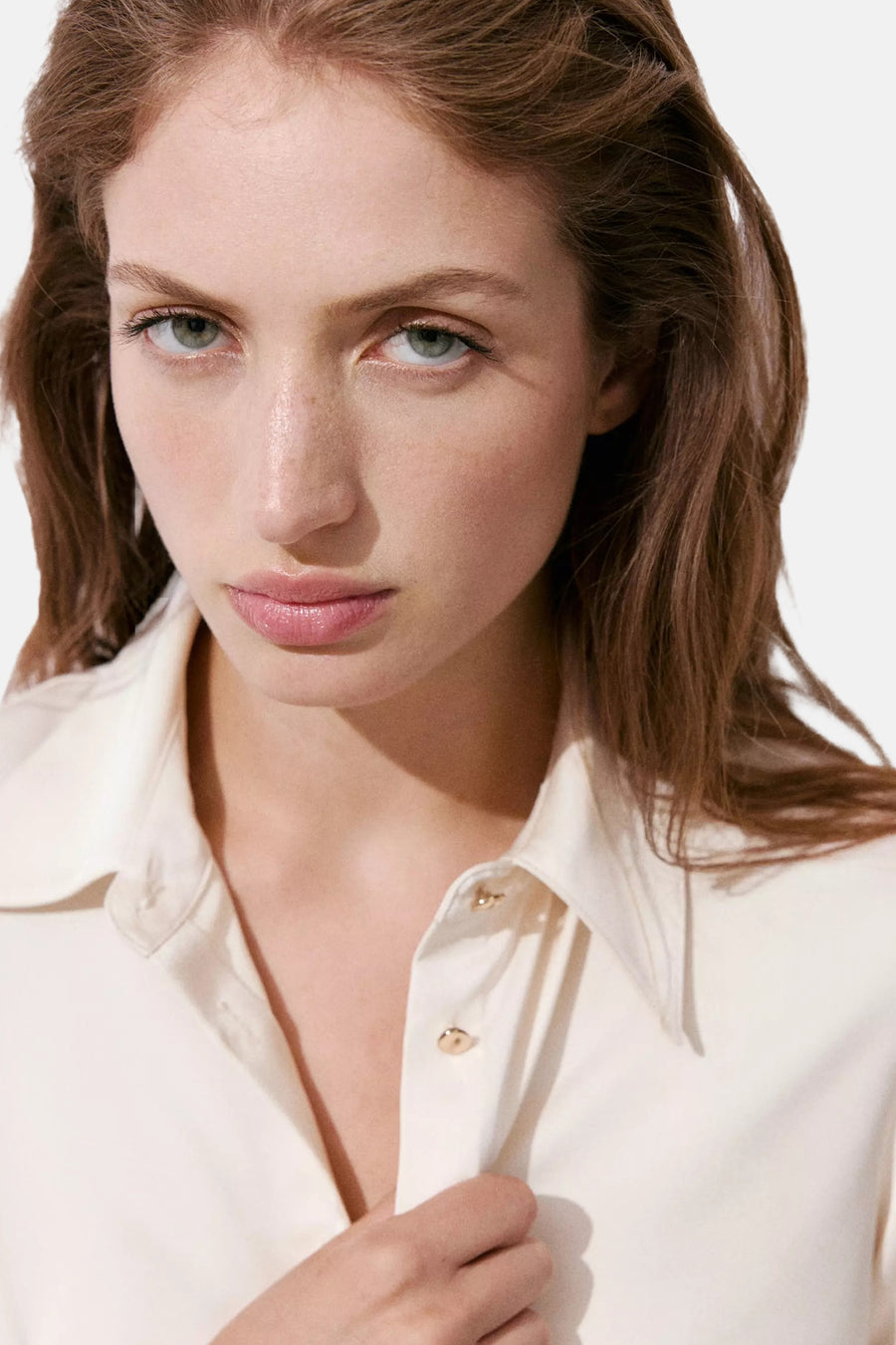 Ecru long-sleeve blouse with pointed collar and gold buttons, close-up front view on model