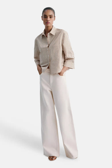 Multicolored short-sleeve blouse with vertical stripes and front pocket, worn with wide-leg cream trousers in a full-length lifestyle view