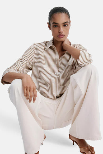Multicolored short-sleeve blouse with vertical stripes and subtle dot pattern, worn with white wide-leg pants and brown heels, lifestyle front view