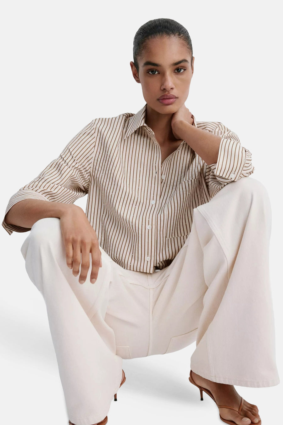Multicolored short-sleeve blouse with vertical stripes and subtle dot pattern, worn with white wide-leg pants and brown heels, lifestyle front view