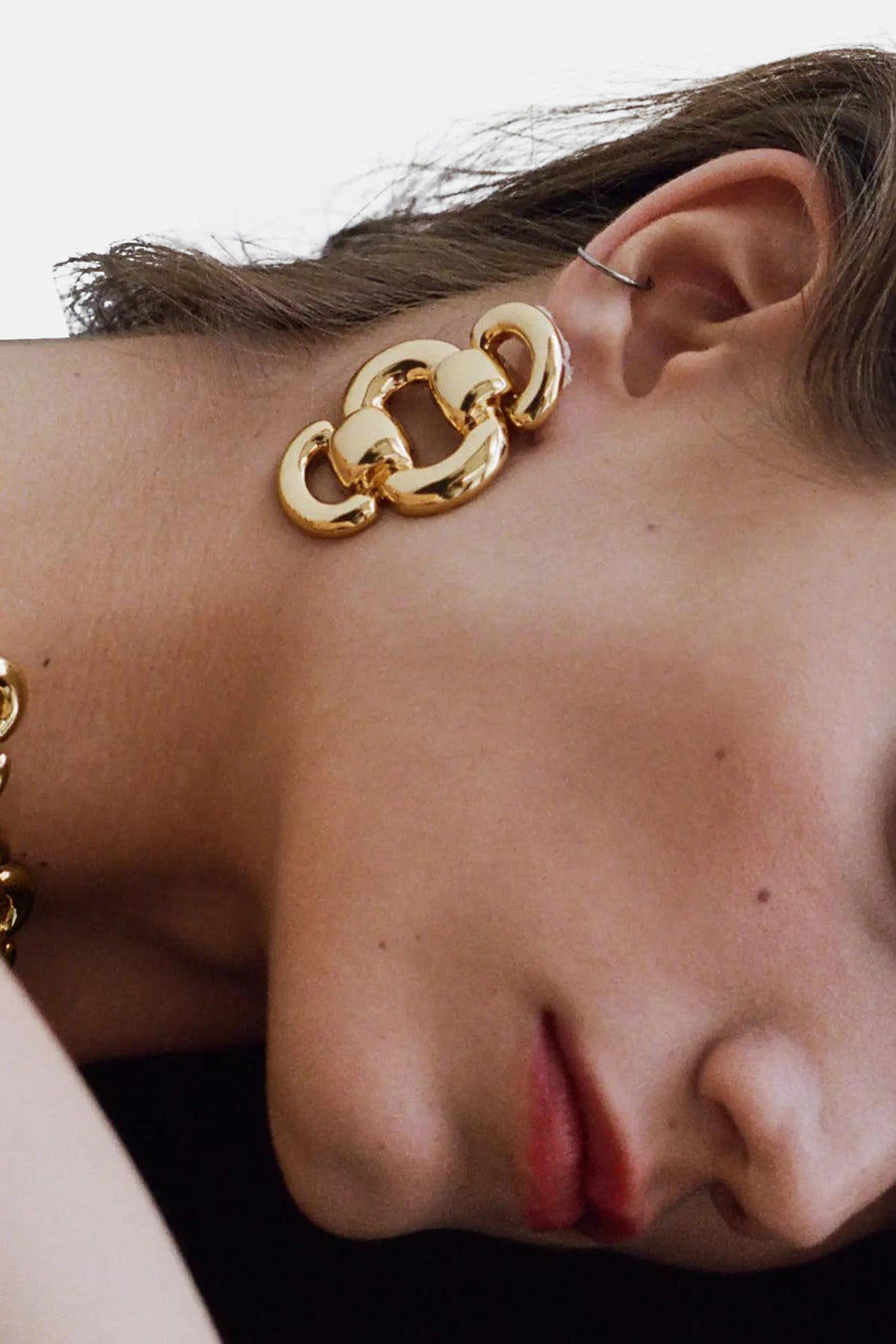 Gold chain-link earrings with polished finish, side view on model, featuring large interlocking loops and ear piercing detail