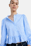 Light blue long-sleeve blouse with floral texture and ruffled hem, worn with dark jeans, front view