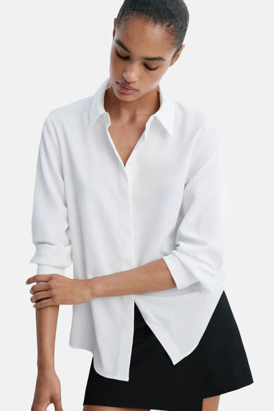 White long-sleeve blouse with pointed collar and button front, worn with black skirt, side view