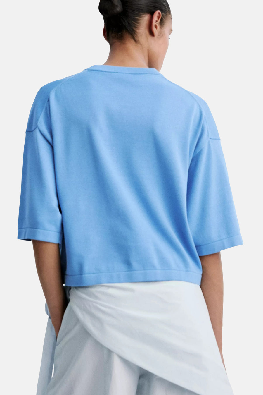 Blue short-sleeve women's sweater back view, soft knit fabric, relaxed fit, worn with white pants