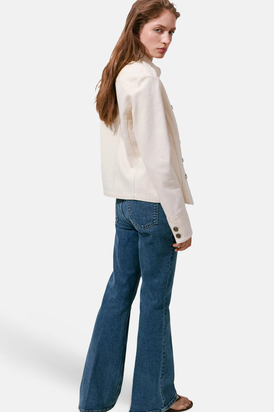 Mid blue flared denim jeans by VIOLETA, side view, worn with cream jacket and sandals