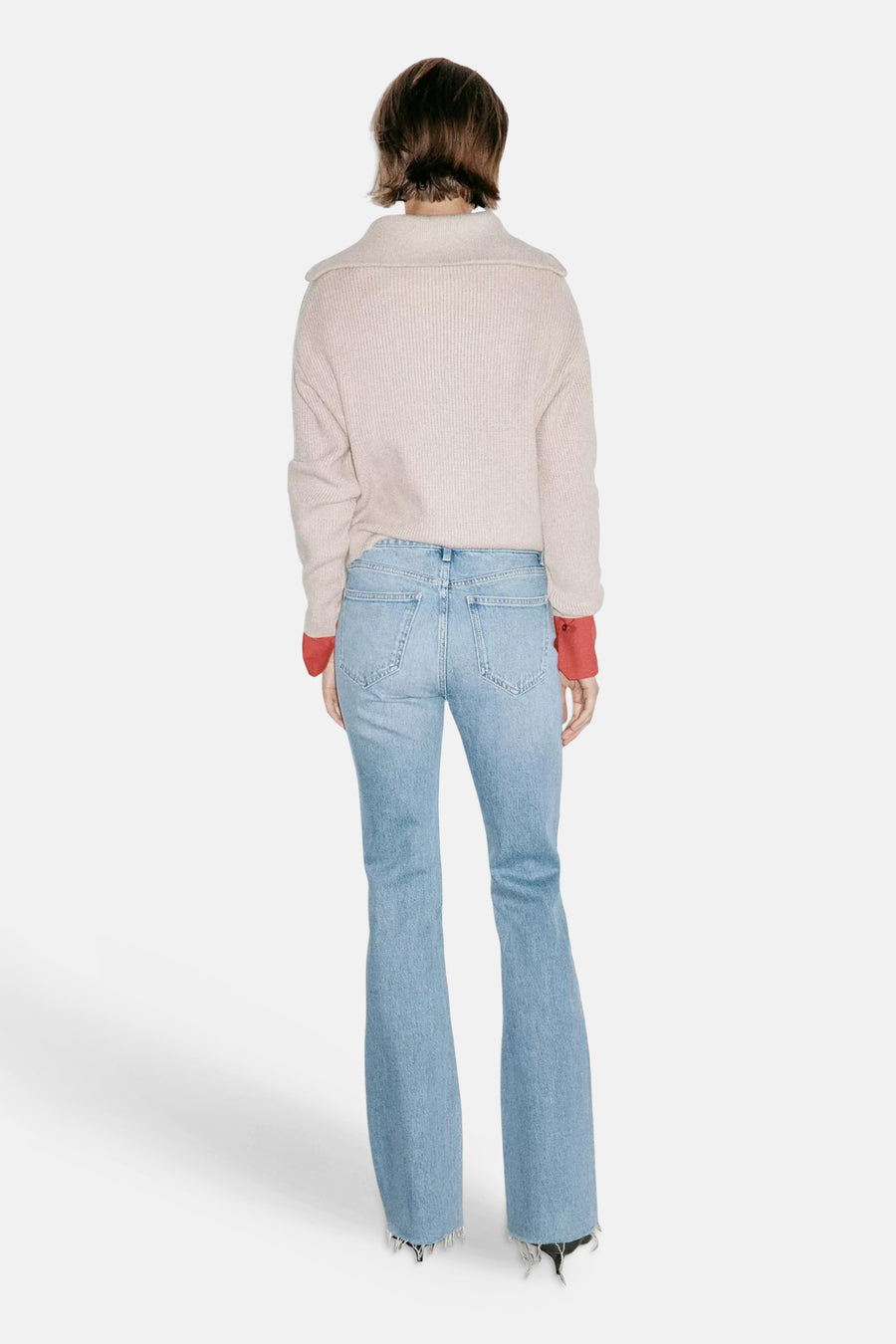 Light blue flared jeans by FIONA, back view, frayed hem, worn with cream ribbed sweater and red cuffs
