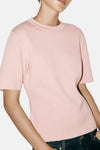 Soft pink short-sleeve knit top with round neckline, worn with dark denim jeans, front view.