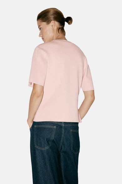 Soft pink short-sleeve knit top with ribbed texture, back view on model wearing dark denim jeans