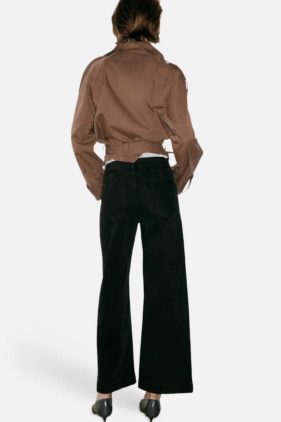 Black wide-leg denim jeans by Catherin, back view, featuring classic stitching and cuffed hems, worn with a brown jacket and black heels.