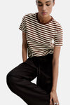 Multicolored short-sleeve striped t-shirt with brown and cream horizontal stripes, crew neck, worn by model in lifestyle pose with black pants.