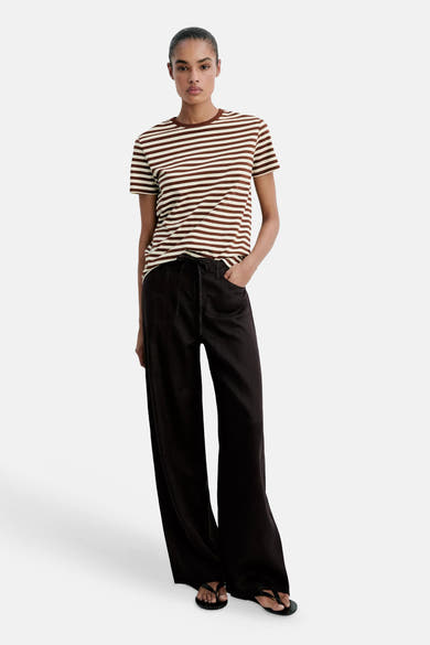 Multicolored short-sleeve striped T-shirt with brown and cream horizontal bands, worn with black wide-leg pants and flip-flops, front view.