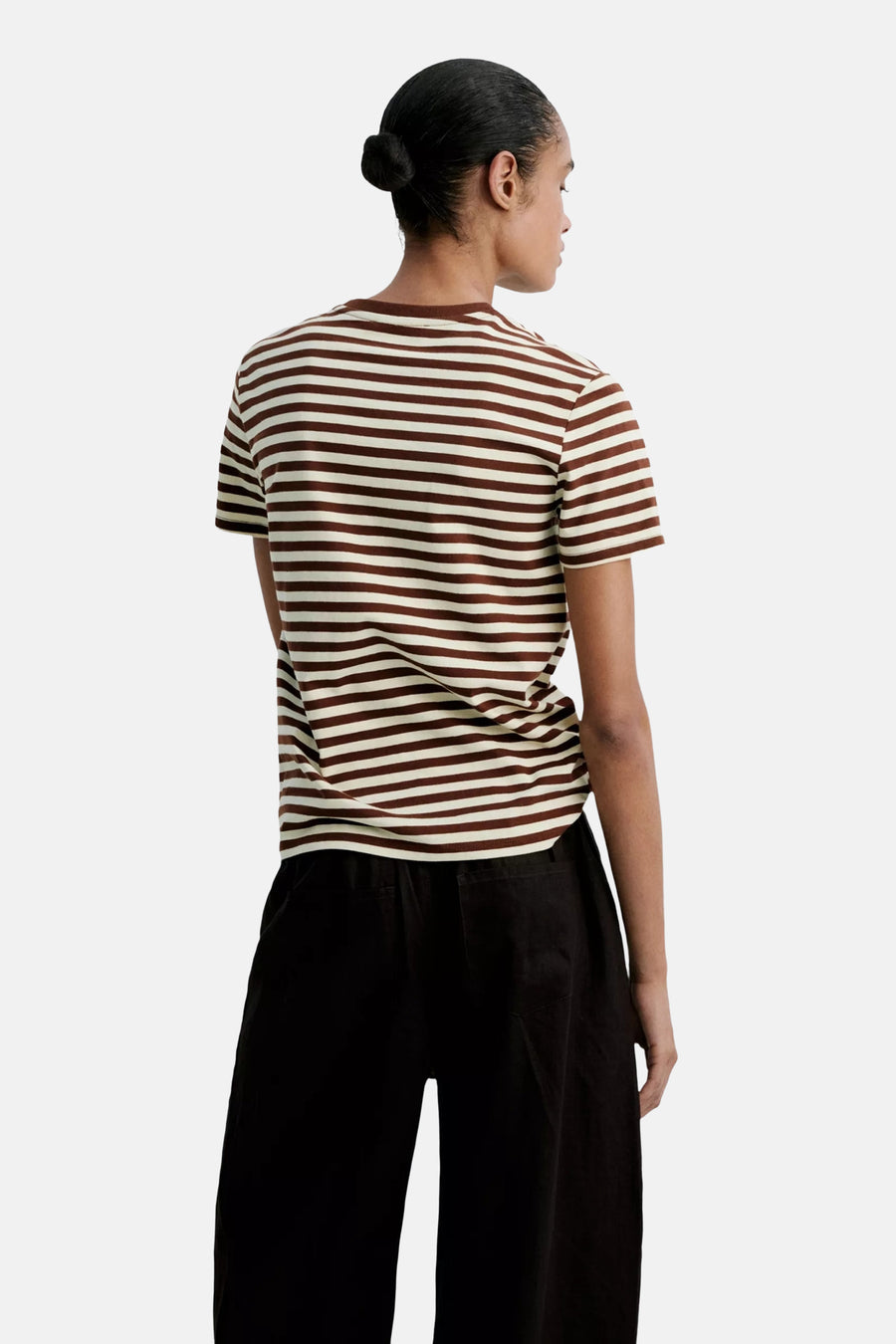Multicolored short-sleeve striped T-shirt with brown and cream horizontal bands, shown from back on model wearing black wide-leg pants