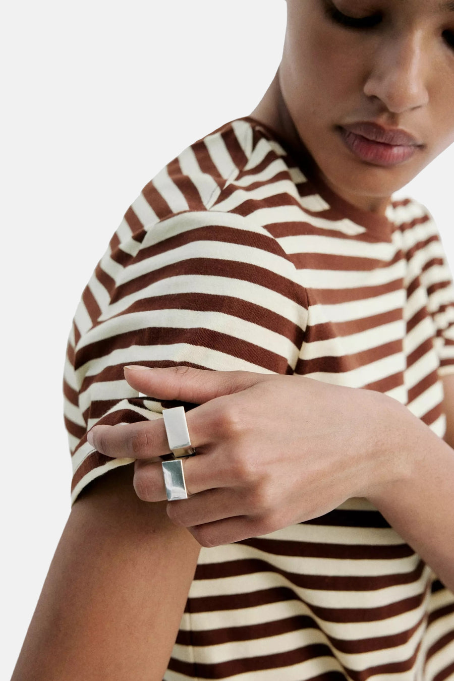 Multicolored short-sleeve t-shirt with brown and cream horizontal stripes, shown in close-up side view on model wearing silver rings.