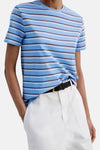 Multicolored short-sleeve t-shirt with blue base and brown-white stripes, worn with white pants and black belt, front view