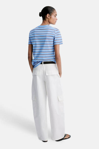 Multicolored striped short-sleeve t-shirt from back view, light blue with brown and white stripes, knotted hem, worn with white cargo pants and black sandals