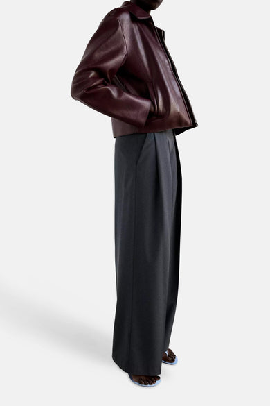 Grey wide-leg formal trousers with front pleats, side view, worn with burgundy leather jacket and blue sandals