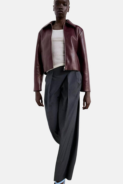 Grey wide-leg formal trousers with pleated front, worn with burgundy leather jacket and white ribbed top, full-length front view
