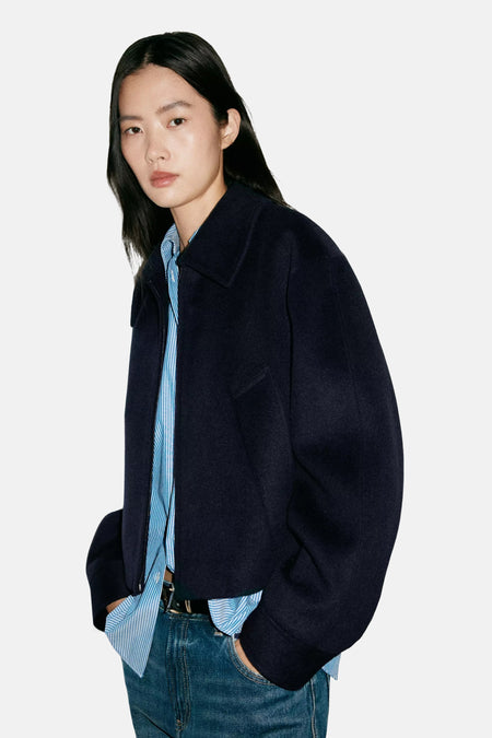 Veste bleu marine en tissu texturé par MANGO, vue de profil, avec col montant et poches, portée sur chemise rayée et jeans.