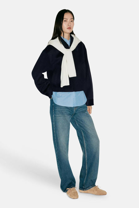 Veste bleu marine à col foulard blanc par MANGO, portée avec chemise à rayures et jeans larges, vue de profil.