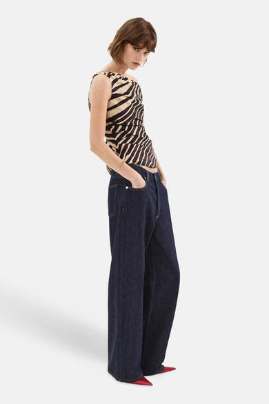 Multicolored sleeveless blouse with black and cream zebra print, side view on model wearing dark wide-leg jeans and red pointed-toe shoes