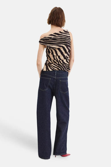 Multicolored sleeveless blouse with black and beige zebra print, back view, worn with dark denim pants and red heels