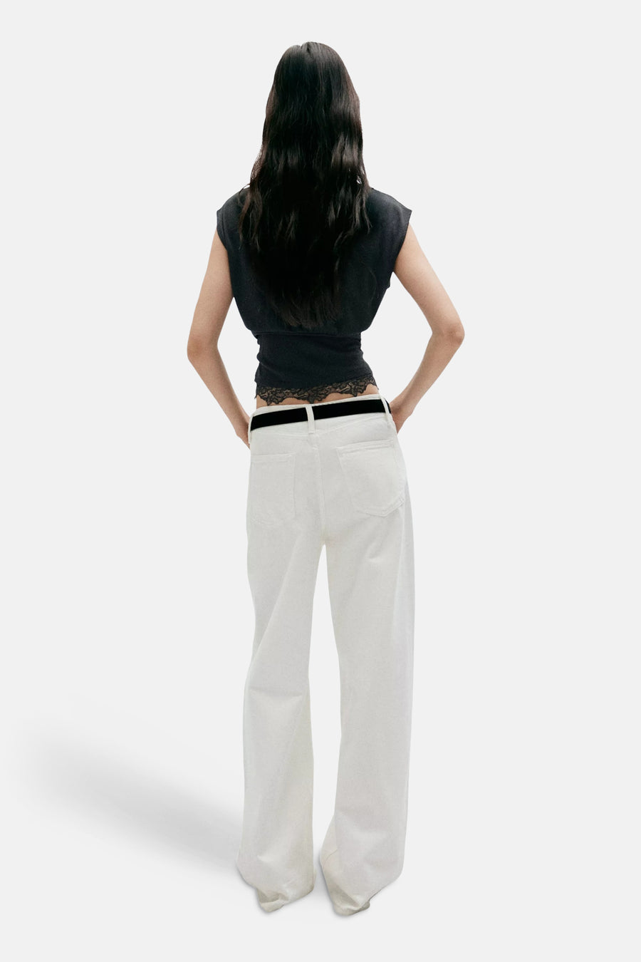 Black sleeveless top with ribbed texture and cropped fit, back view showing lace trim at hem, worn with white wide-leg pants and black belt.