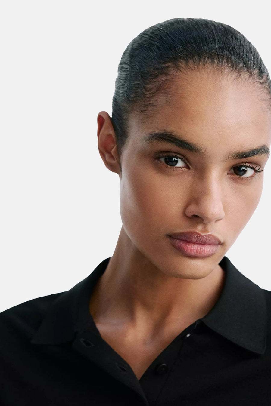 Black short-sleeve polo shirt with classic collar and button placket, worn by model in close-up front view