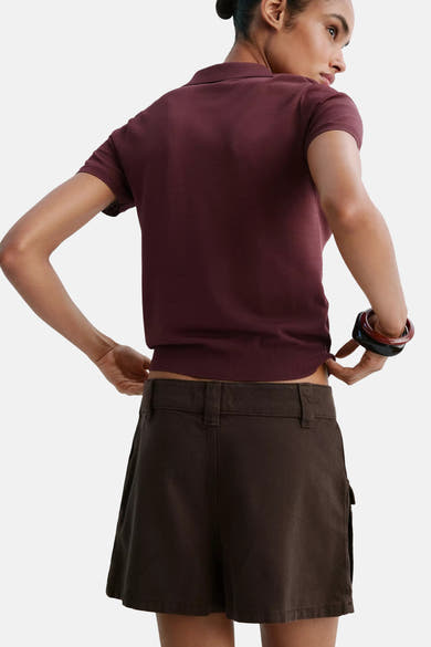 Bordeaux short-sleeve polo shirt with ribbed collar and hem, shown from back on model wearing dark shorts and stacked bangles.