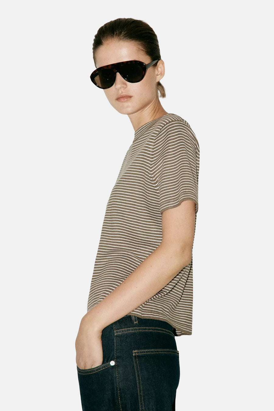Kaki short-sleeve striped knit top with white horizontal stripes, side view on model wearing dark jeans and sunglasses