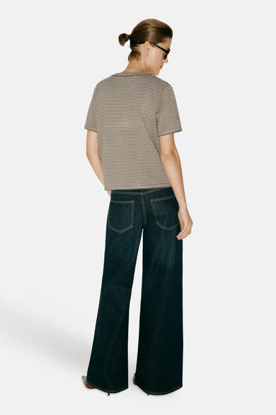 Kaki short-sleeve sweater with white horizontal stripes, back view, worn with dark wide-leg jeans and sunglasses