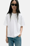 White short-sleeve t-shirt with relaxed fit and round neckline, worn by model in lifestyle front view with blue jeans and sunglasses.