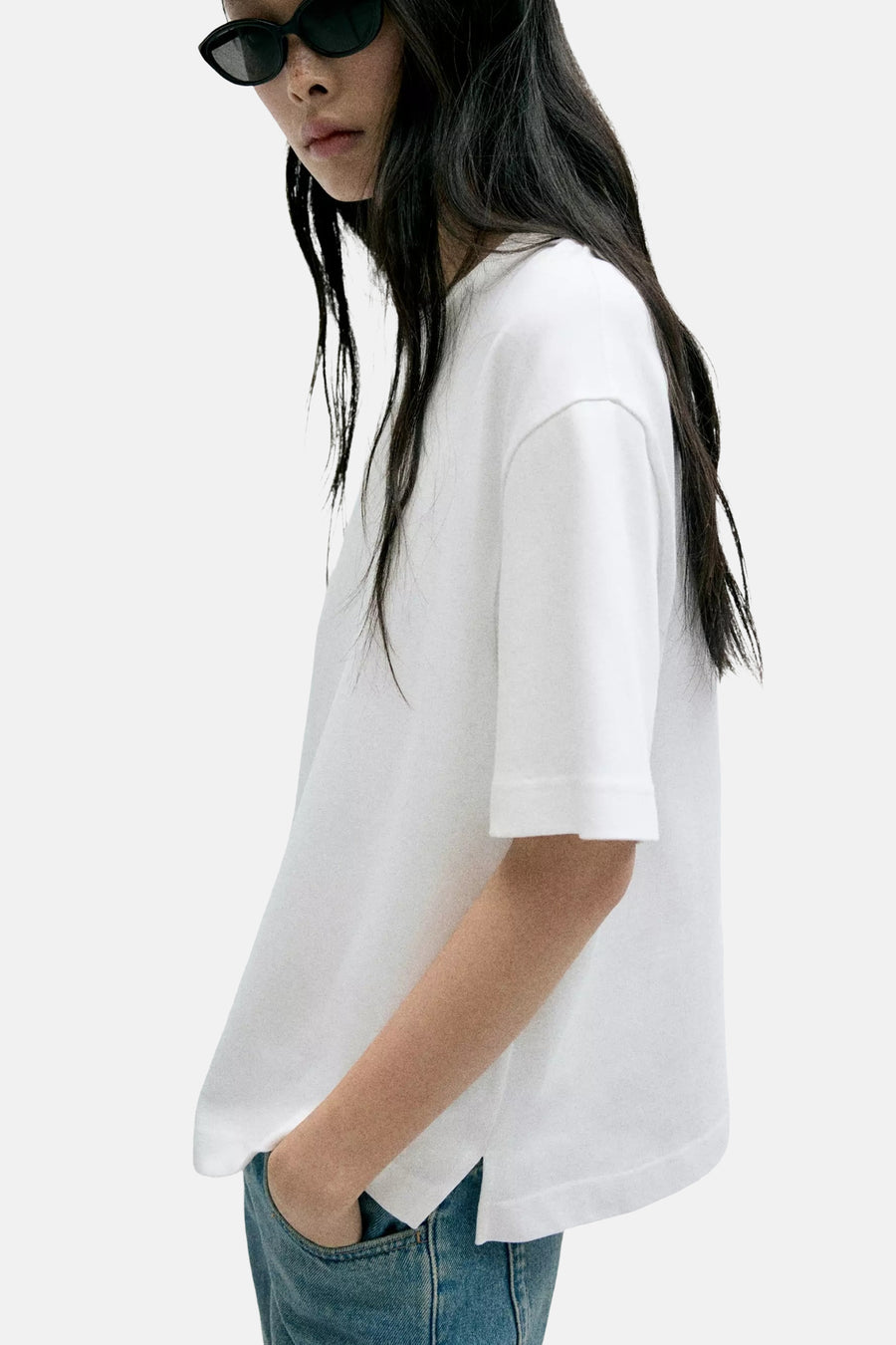 White short-sleeve t-shirt with relaxed fit and rounded hem, side view on model wearing jeans and sunglasses