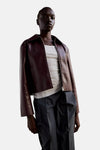 Bordeaux leather jacket with front zipper and collar, worn over white ribbed top and dark trousers, front view