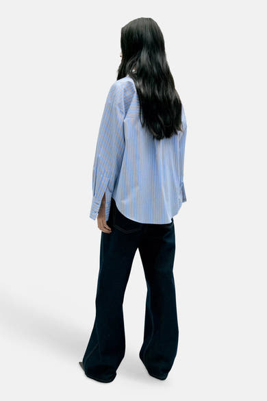 Blue long-sleeve striped blouse with relaxed fit, back view, worn with dark flared jeans
