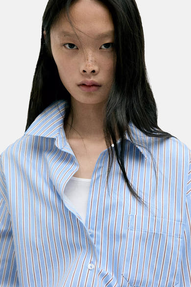 Blue striped long-sleeve blouse with white and red vertical stripes, button-down front, chest pocket, worn over white top, close-up front view