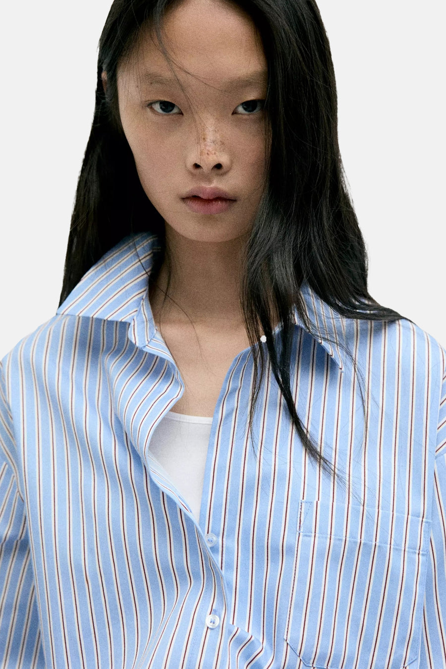 Blue striped long-sleeve blouse with white and red vertical stripes, button-down front, chest pocket, worn over white top, close-up front view