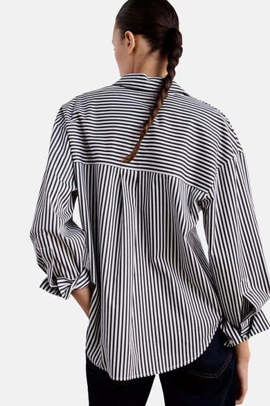 Black and white striped long-sleeve blouse with pleated back, shown from rear on model wearing dark jeans